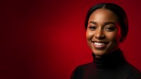 Young African American woman smiling warmly in black turtleneck against red background for professional headshots and business portraits.