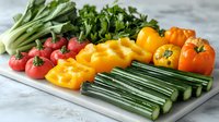 Fresh colorful vegetables arranged in rows on marble board including radishes, yellow and orange bell peppers, celery stalks and leafy greens for healthy eating.