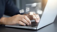 Person typing on laptop with digital email icons floating above keyboard, representing electronic communication and modern business correspondence.