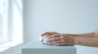 Hands holding white ceramic mug on minimalist table by window with natural light for morning coffee break relaxation and mindfulness moments.