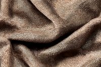 Natural linen fabric with textured weave pattern in brown tones, showing soft folds and wrinkles. Close-up macro photography reveals detailed textile structure.