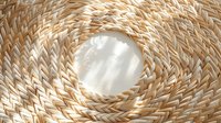 Circular woven natural straw pattern with sunlight and shadows creating depth and texture. Close-up view of traditional handcraft material for home decor and accessories.
