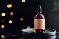 Amber glass bottle with pump dispenser on black stone plate against dark background with golden bokeh lights, minimal luxury cosmetic packaging design.
