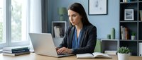 Professional businesswoman working on laptop at modern office desk with natural lighting and organized workspace for corporate productivity.
