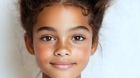 Young mixed race girl with curly dark hair and bright smile against white background, natural beauty portrait showing genuine happiness and confidence.