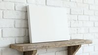 Blank white canvas on rustic wooden shelf against white brick wall background for art projects and creative displays.