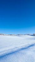 Frozen lake landscape with snow-covered surface, distant frost-covered trees, and clear blue sky. Winter scenery suitable for seasonal campaigns, travel promotions, and nature-themed designs.