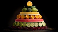 Colorful fruit and vegetable pyramid arrangement on dark background showcasing healthy nutrition diet concept with fresh organic produce layers.
