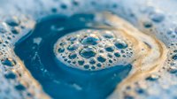 Blue liquid soap foam with bubbles swirling in a spiral pattern, macro close-up texture for cleaning, hygiene, and household product concepts.