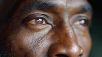 Close up portrait of African American man with intense gaze and expressive brown eyes against dark background, showing genuine emotion and strength in dramatic lighting.