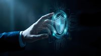 Businessman hand touching glowing digital shield icon with circuit patterns representing cybersecurity protection and data safety technology concept.