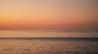 Serene ocean sunset with golden orange sky reflecting on calm water surface creating peaceful horizon seascape for meditation and relaxation backgrounds.