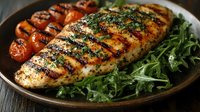 Grilled chicken breast with herb seasoning served on bed of fresh arugula with roasted cherry tomatoes on rustic plate, showcasing grill marks and caramelization.