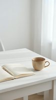 Minimalist workspace with open book and ceramic coffee cup on white desk in bright natural light for productivity and reading concepts.