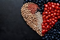 Heart shape made from various legumes and fresh cherry tomatoes on black background. Healthy eating concept featuring chickpeas, lentils, black beans and tomatoes.