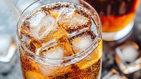 Refreshing cola drink with ice cubes in glass, fizzy brown carbonated soda with bubbles and condensation drops, selective focus on dark background.