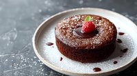 Decadent chocolate lava cake with molten center topped with fresh raspberry and powdered sugar, served on ceramic plate against dark background.