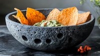 Crispy tortilla chips with fresh guacamole served in traditional stone molcajete bowl on dark background, perfect for Mexican cuisine appetizer.