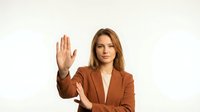 Professional businesswoman in brown suit making stop gesture with raised hand on white background for corporate presentations.
