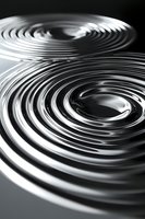 Abstract metallic spiral waves creating dynamic circular patterns with reflective chrome surface and dramatic lighting effects for modern design projects.