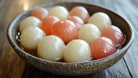 Colorful traditional Asian glutinous rice balls in ceramic bowl on wooden table. Sweet dessert dumplings for festivals and celebrations.