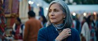 Mature Caucasian woman with gray hair shopping at evening market, looking thoughtful while browsing stalls with warm bokeh lights in background.