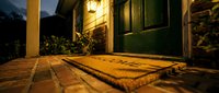 Welcome home doormat on a brick porch at night, glowing lantern above a green front door creating a warm, inviting entrance.