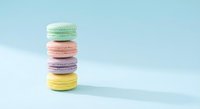 Colorful French macarons stacked on pastel blue background. Sweet dessert cookies in mint green, pink, purple and yellow colors for bakery menu design.