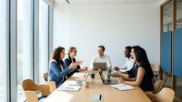 Professional business team meeting in modern conference room with laptops and documents discussing strategy and collaboration in bright office space.