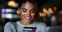 Young mixed race woman smiling while shopping online with credit card in cozy evening atmosphere with bokeh lights. Modern lifestyle and e-commerce concept.