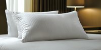 Soft white pillows on hotel bed with crisp linens against warm ambient lighting, creating cozy and luxurious atmosphere for hospitality and comfort concepts.