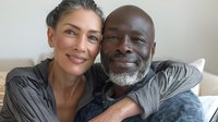 Mature interracial couple embracing on sofa, smiling at camera. Authentic representation of loving relationship for lifestyle and relationship content.
