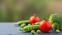 Fresh organic vegetables including ripe red tomatoes, green peas in pods, and broccoli arranged on dark surface with natural blurred background for healthy eating.