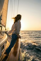 Young woman enjoying sunset sailing adventure on luxury yacht deck with wind in hair and ocean waves splashing around boat during golden hour cruise.