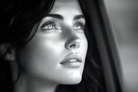Young woman with striking eyes gazing upward in dramatic black and white portrait. Natural lighting creates ethereal highlights on face. Artistic fashion photography.