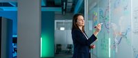 Professional businesswoman presenting data analytics on interactive digital display in modern corporate office environment for strategic planning meetings.