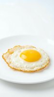 Fresh fried egg with golden yolk on white plate against clean background for breakfast menu and cooking content.