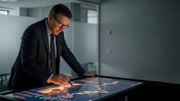 Middle-aged Caucasian businessman in suit analyzing financial data on interactive touchscreen table in modern office environment for strategic planning.