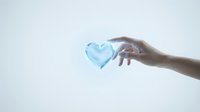Hand reaching toward glowing blue heart symbol representing love, care, compassion and emotional connection on clean white background for wellness concepts.