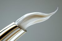 Elegant white cream swirl emerging from silver cosmetic tube against neutral gray background, showcasing luxury skincare product texture and consistency.