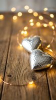 Silver heart ornaments with warm fairy lights on rustic wooden background creating romantic holiday atmosphere for seasonal decorations and celebrations.