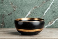 Black ceramic bowl with golden rim and stripe detail on marble counter against green marble wall background, modern minimalist tableware styling.
