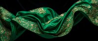 Luxurious emerald green silk fabric with ornate golden paisley pattern flowing elegantly against dark background for premium textile and fashion design projects.