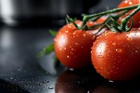 Fresh ripe red tomatoes on vine with water drops against dark background, macro shot showing texture and natural moisture for food photography.