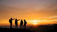 Silhouetted hikers stand together on mountain ridge at golden sunset, ideal for travel, adventure, teamwork, and outdoor lifestyle marketing campaigns.