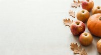 Autumn harvest composition with fresh apples, pumpkin and dried oak leaves on neutral beige background with copy space for seasonal marketing materials.