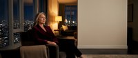 Professional blonde businesswoman in burgundy blazer sitting confidently in luxury office with city skyline view at night, corporate executive lifestyle.