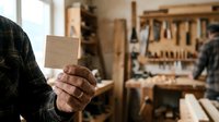 Craftsman holding wooden block in workshop with tools and workbench in background, carpentry and woodworking craft.