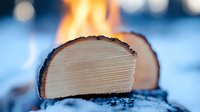 Sliced cheese with melted top and charred crust resting on snow-covered surface with blurred fire and winter landscape background.