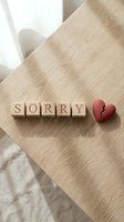 Wooden letter blocks spelling SORRY next to a broken red heart on a light wood table, conveying apology, regret, and relationship conflict.